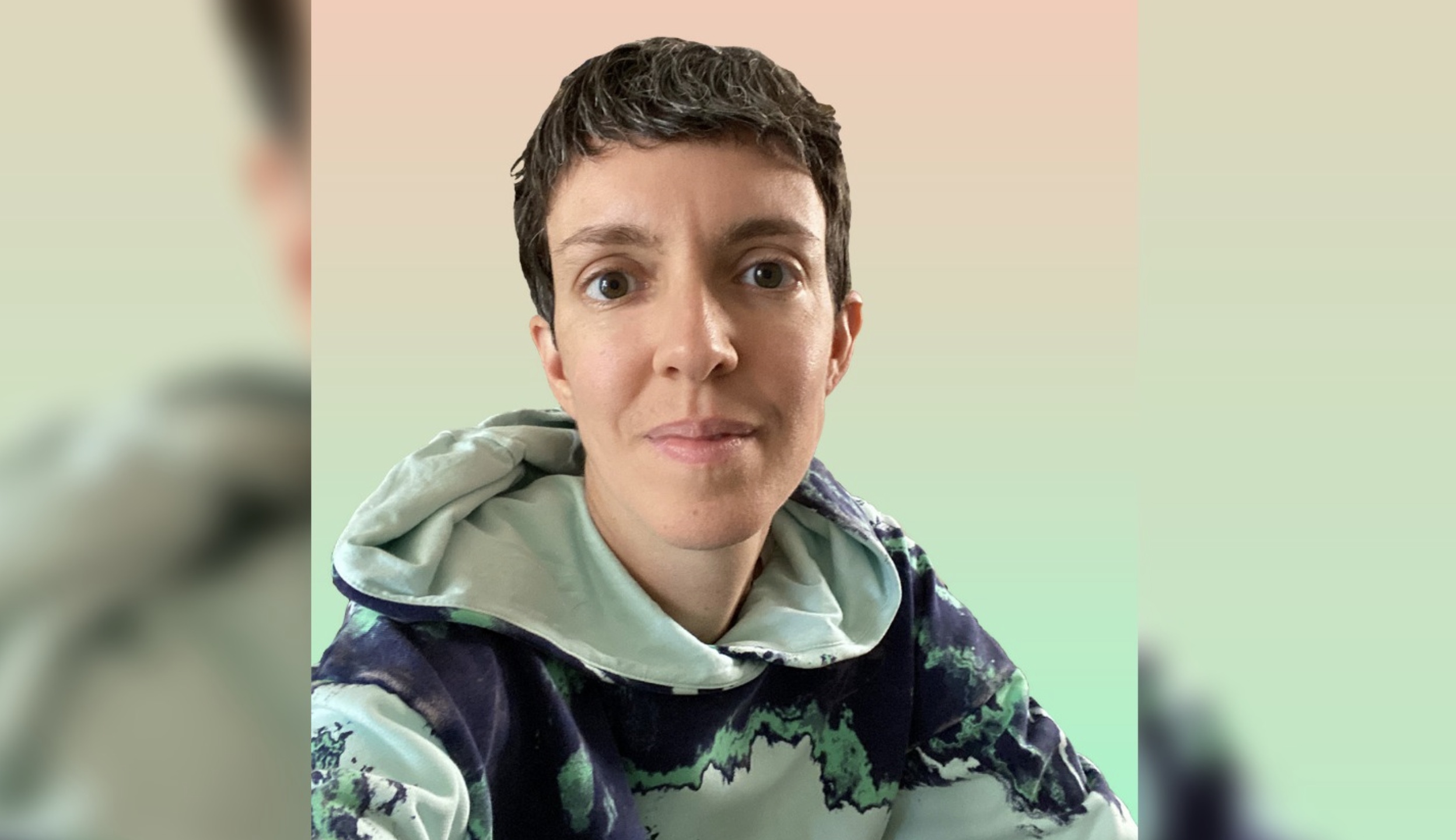portrait of a white, gender-ambiguous person, with short brown hair, hazel eyes, and a warm smile. they are wearing a hoodie with an all-over-print of a synthetic-sliced-mineral-looking, acid pattern that is seafoam green, light cyan, and navy blue. behind them is an artificial background gradient that is peach at the top and seafoam green at the bottom. #acidtropical