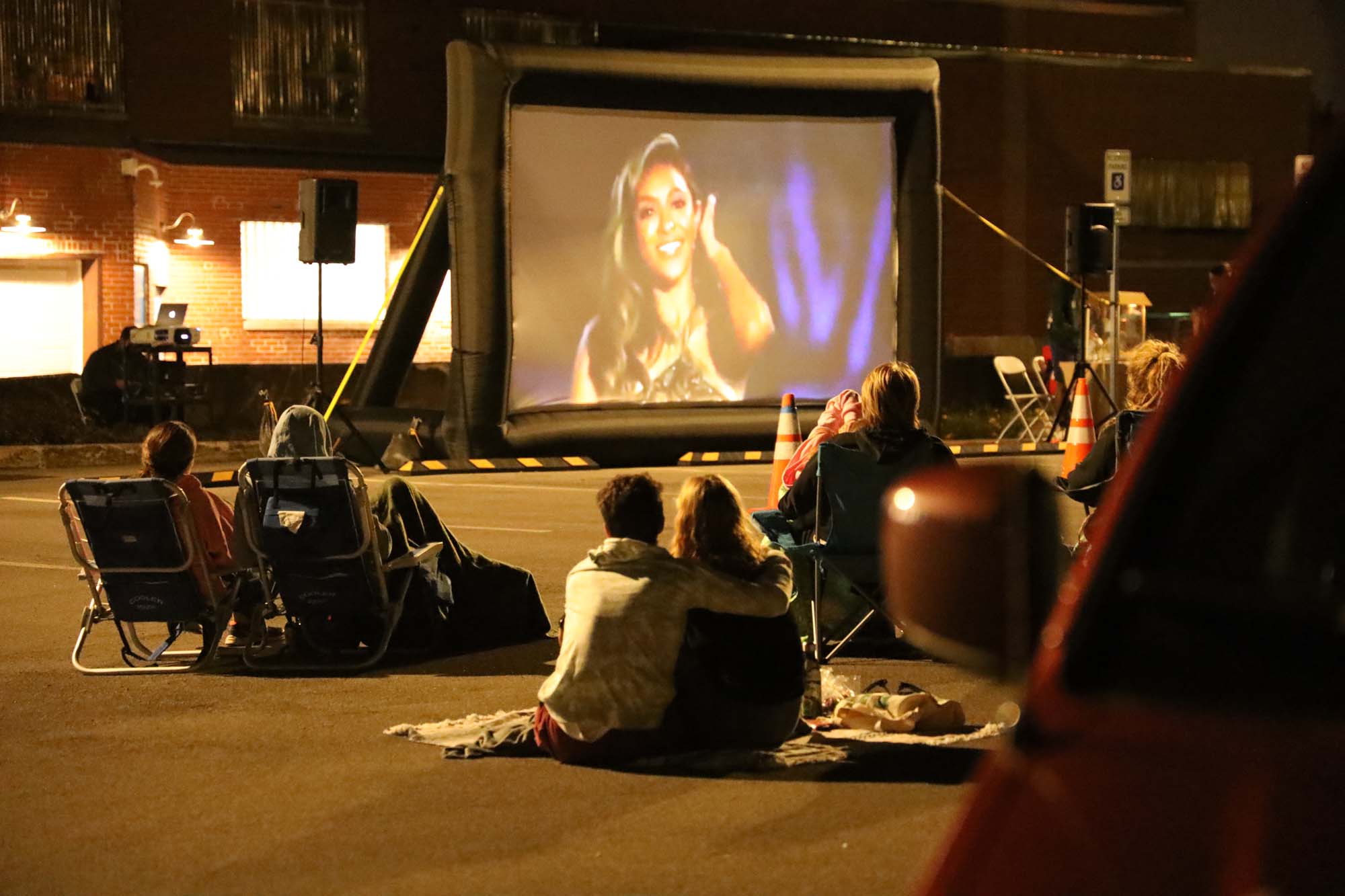 Two people sitting on a blanket outdoors and watching a screen at night. Photograph by Kaitlyn Lowe.