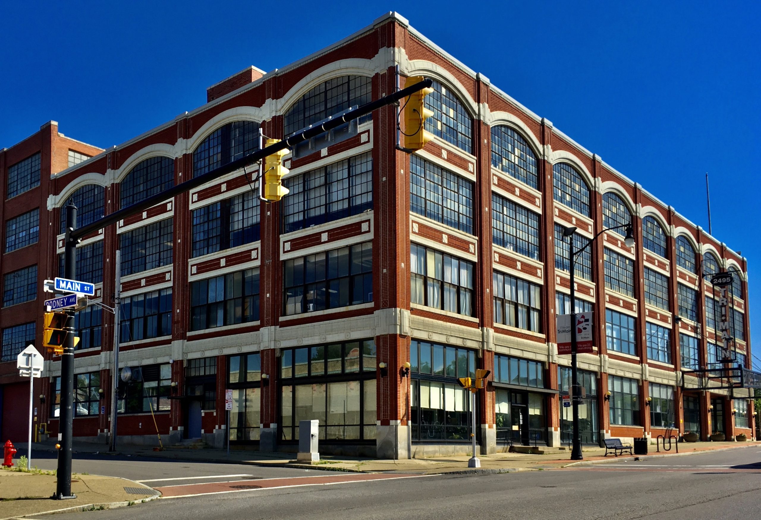A photograph of the Tri-Main Center by Andre Carrotflower. The Tri-Main Center, 2495 Main Street at Rodney Avenue, Buffalo, New York, June 2020. Constructed in 1915, the building is a textbook example of the Daylight Factory style of industrial architecture pioneered in the early 20th century by Albert Kahn, where large windows bathed the production floors in natural light thus improving the health and morale of the workers. Originally a Ford assembly plant, the complex was sold to the Trico Corporation after the Second World War and became the second of the three windshield wiper factories operated by that company in Buffalo (the others were located on Goodell and Elk Streets respectively). Trico closed the plant in 1987; it's now a mixed-use complex housing offices, studios, and light industrial facilities.