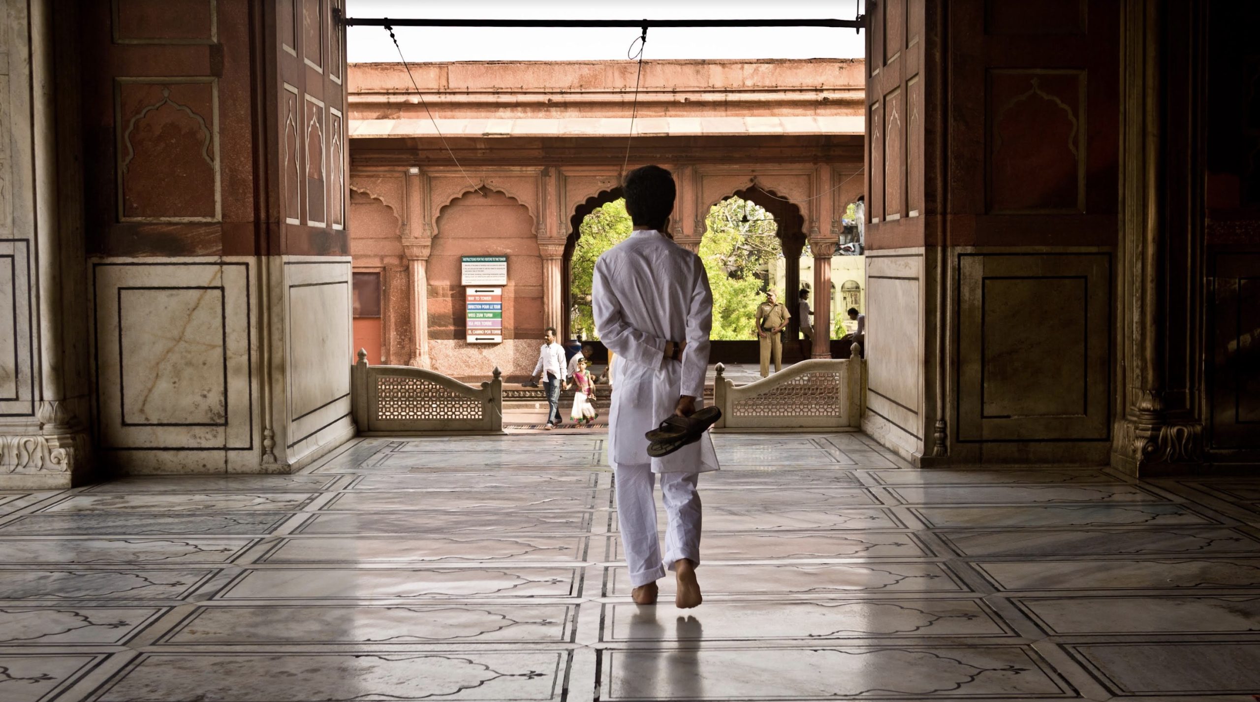 Zain Alam walking with his back to the camera in a partially enclosed area. He is dressed entirely in white.
