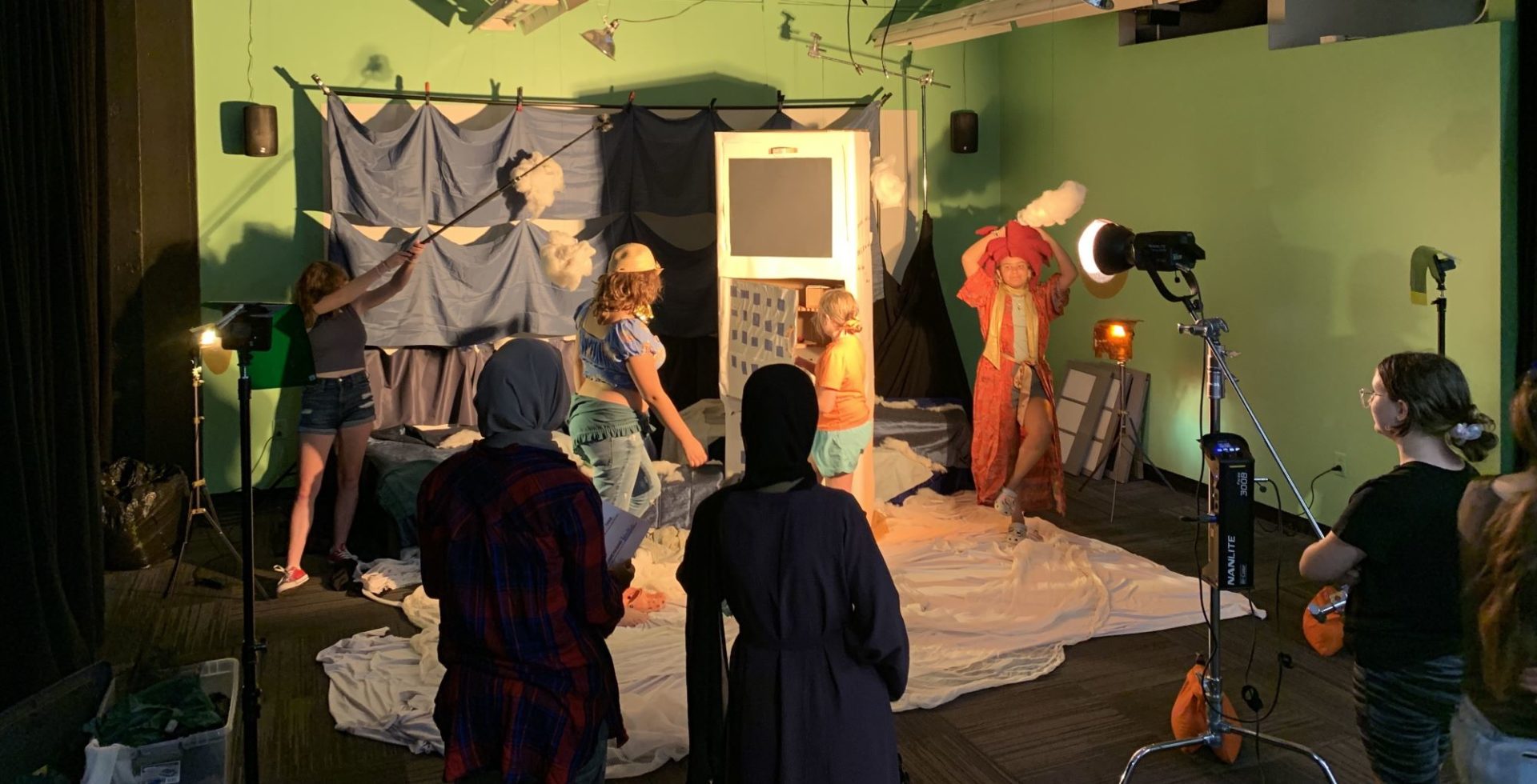 Young people in a film production with a set made of cardboard and cloth Some of them are in costumes, some of them are operating film production equipment. Photograph taken in Avye Alexandres' Video Production: Color and Light summer youth workshop.