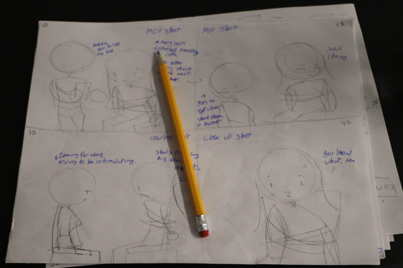 A 4-panel storyboard showing simply drawn figures and dialogue. A wooden pencil lies on top of the paper.